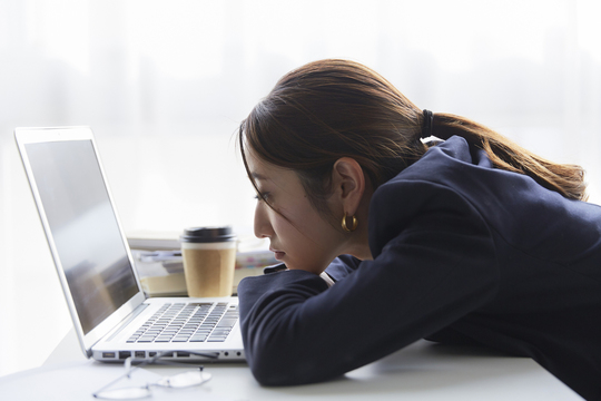 パソコンを見ながら机にもたれる女性